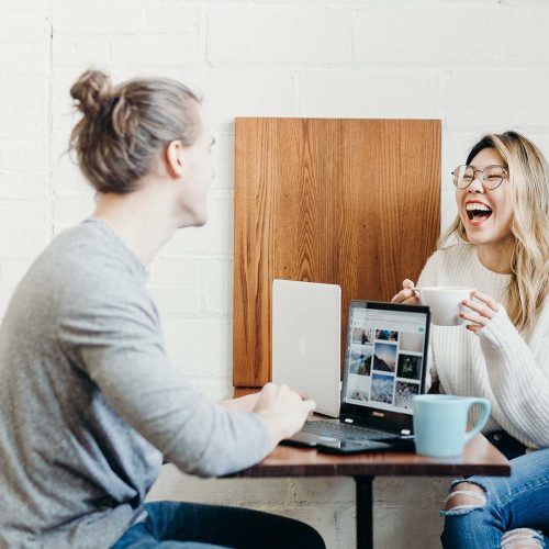 alt="Specialist casually accepting a client order while working on a laptop, with a colleague laughing nearby"